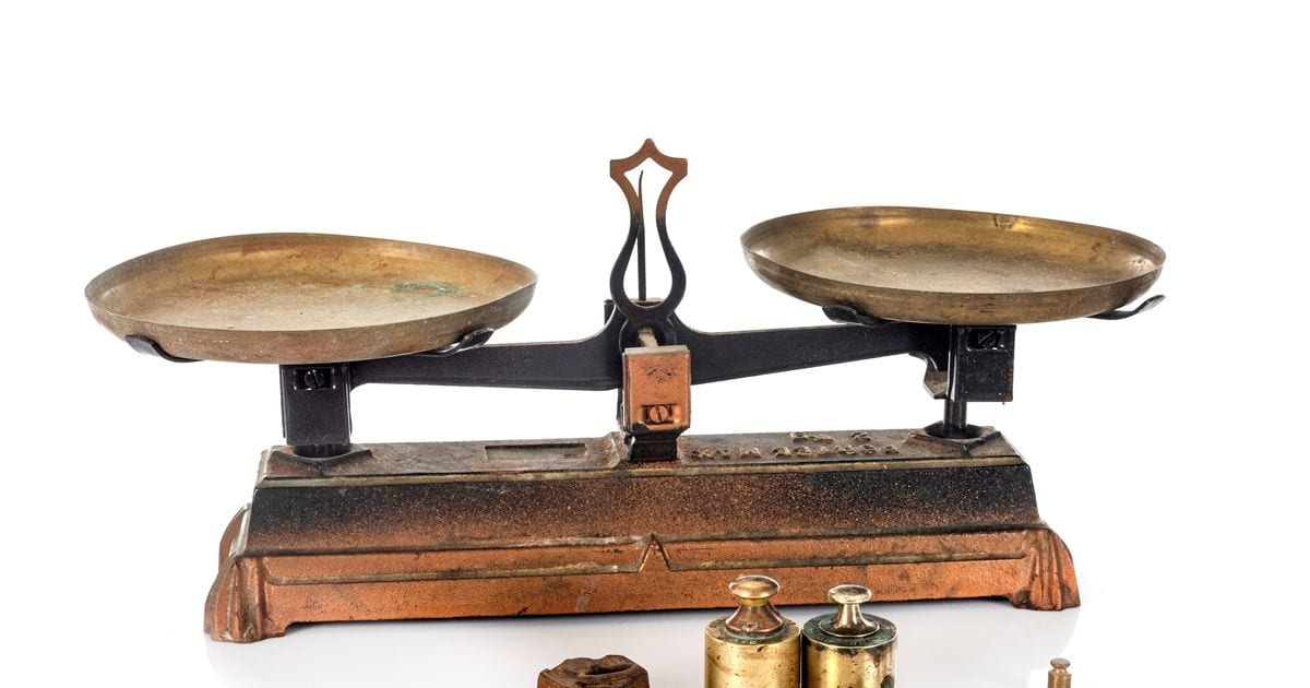 An antique brass balance scale with two empty pans and small weights in front of it