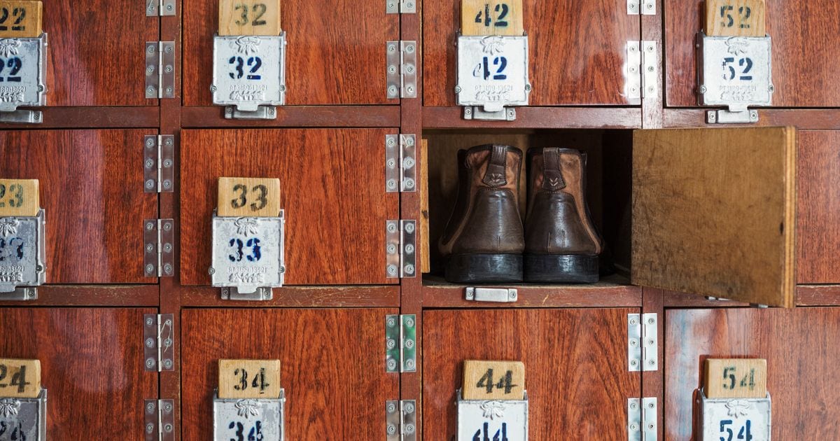 A wall of numbered wooden lockers with one door open and a pair of brown leather boots left inside