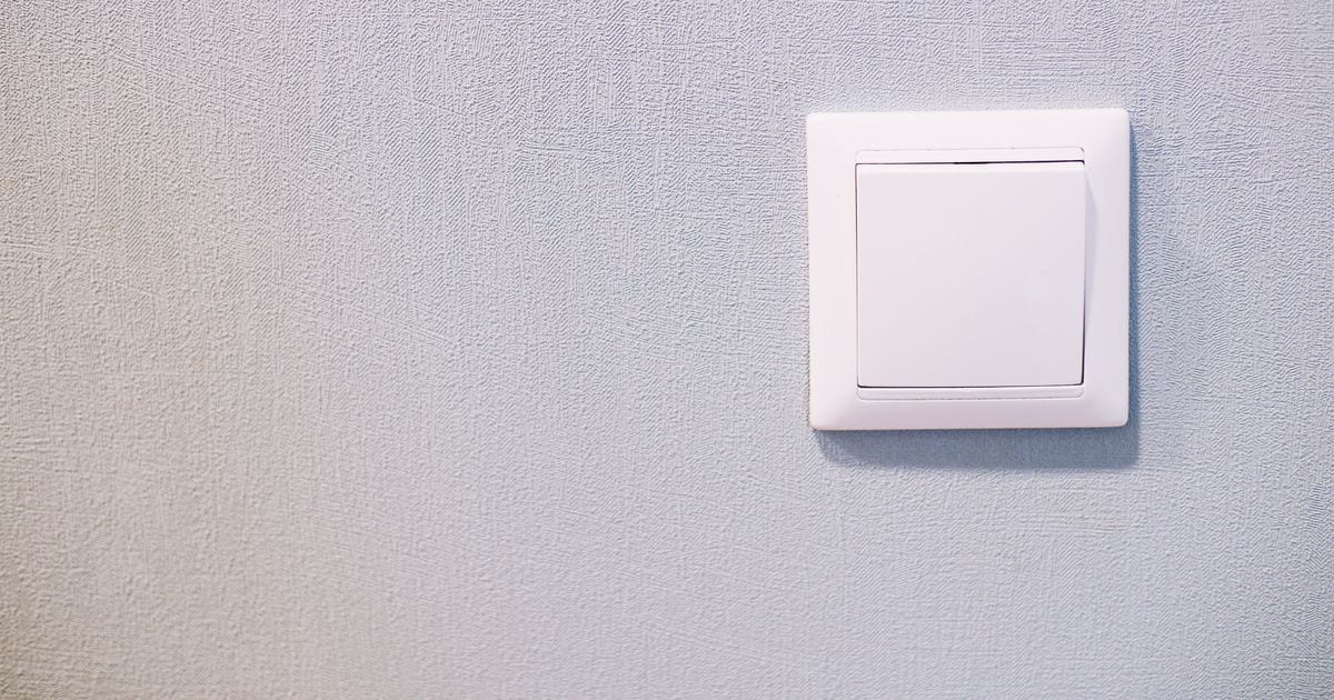 A white light switch on a pale blue textured wall