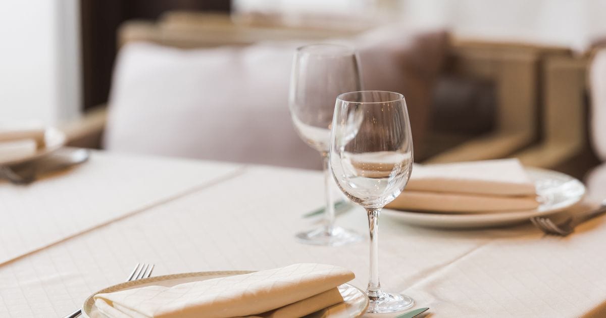 A restaurant table laid with wine glasses, plates and folded napkins before anyone has sat down
