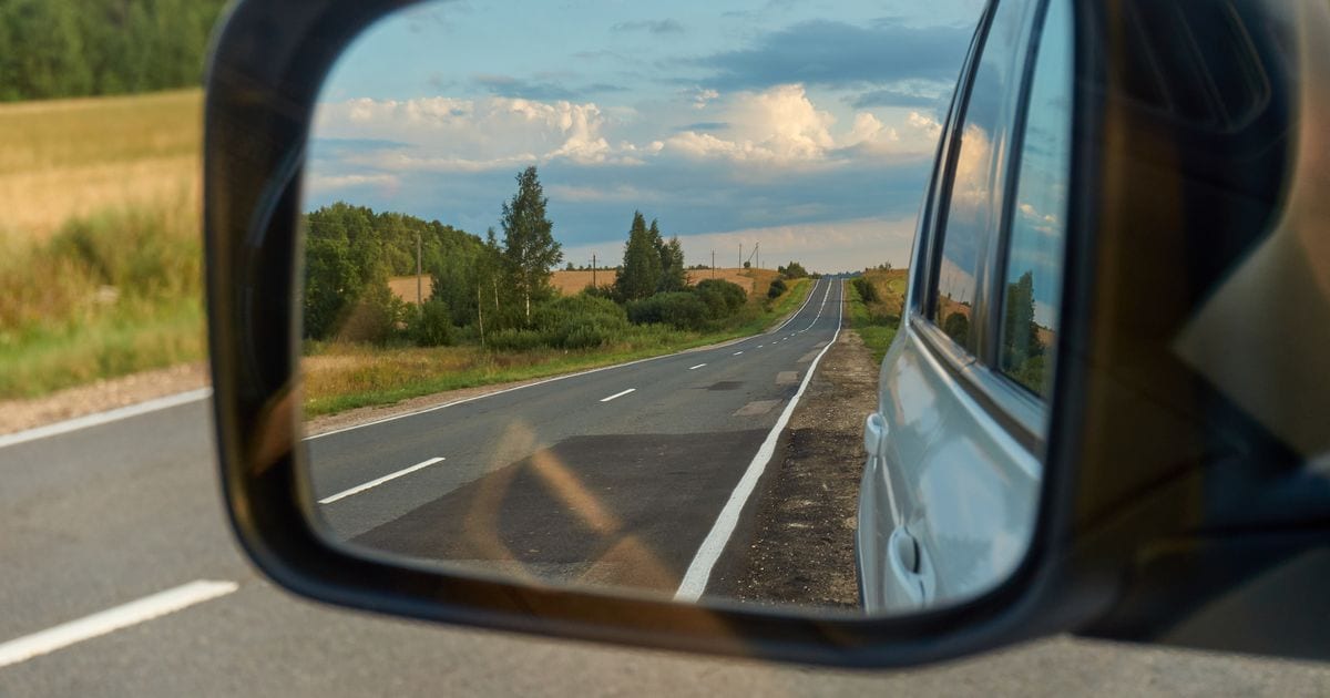 A country road behind a car, seen in the car's side mirror